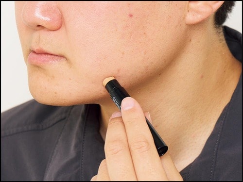 男性が顔にコンシーラーを塗っている様子