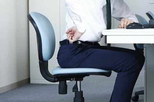 オフィスチェアに座って腰に手を当てる人