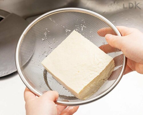 1：パックの水を捨てザルに入れる 木綿豆腐の冷凍保存術おすすめ イメージ